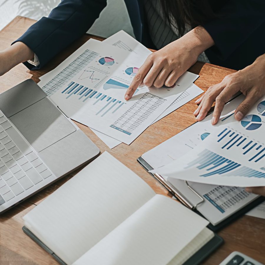 Mãos apontando para relatórios com gráficos sobre a mesa de trabalho